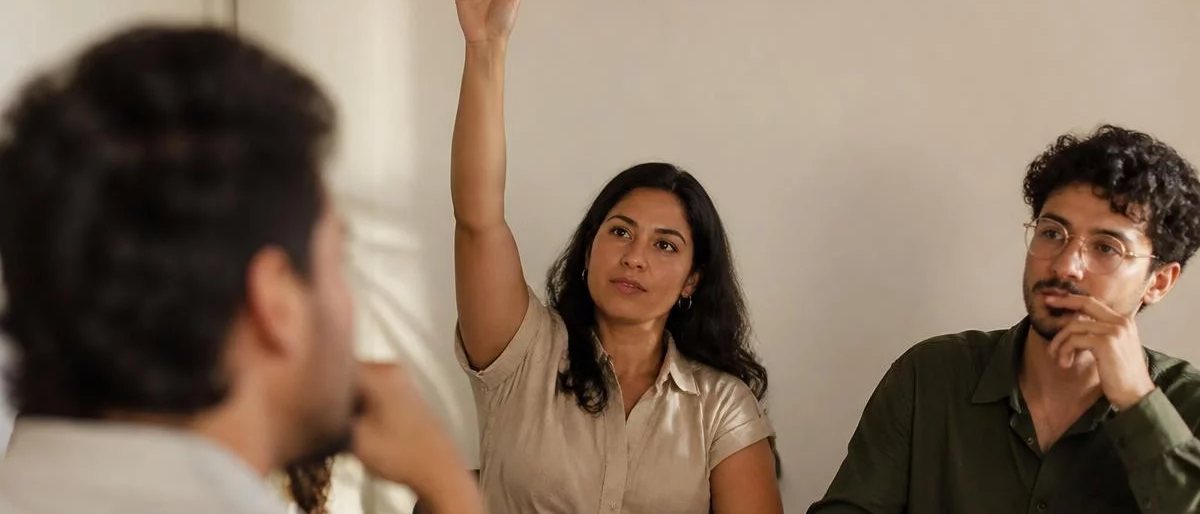 Participante com a mão erguida pedindo a vez, à mesa coberta de folhas escritas